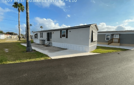 A white mobile home with black trim and a palm tree.